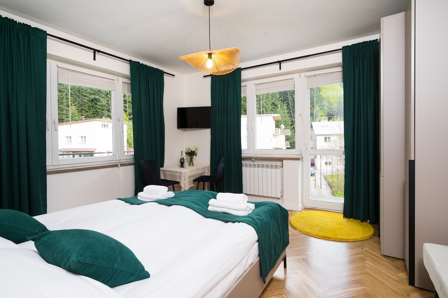 Apartament typu Classic (5) — jasna sypialnia z zielonymi zasłonami i drewnianą podłogą